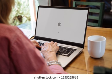 ROSARIO, ARGENTINA - NOVEMBER 16, 2020: Apple logo in the screen of laptop. Mature woman sitting in front of computer with mac os x operating system start screen.