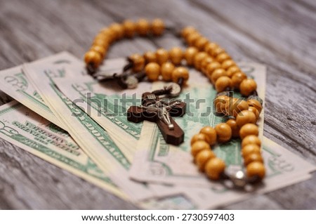 Rosary beads are arranged over a stack of dollar bills on a wooden surface in a common room. The scene shows faith and money together in one view.