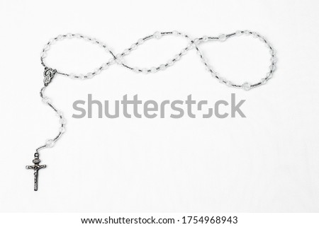 Rosary of the catholic religion with metal cross, metal medal of the Virgin Mary and transparent plastic beads arranged in a inverted shape on the left and upper side of the box, on a white background