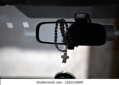 A rosary with a christian cross hangs on a car mirror.