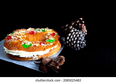 Roscon De Reyes Stuffed With Cream With Black Background And Pine Cones For Christmas, Dessert Or Typical Cake From Spain On Three Kings Day On January 6