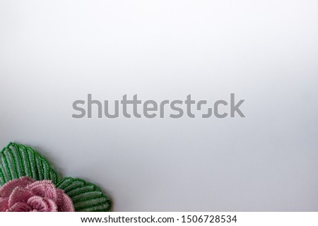 Rose from beads in the lower left corner of the white background. Rose on a white background. Beaded flowers.
