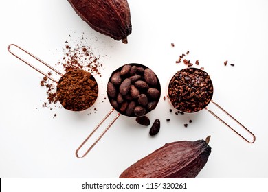Rose gold measuring cups of cocoa beans, cacao nips, cocoa powder and cocoa pods on a white background, flat lay healthy food concept - Shutterstock ID 1154320261