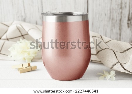 Rose gold wine tumbler with lid mockup with checkered kitchen towel, beige flower, wooden clip on a white wood background. Svg product mockup, drinkware mockup for svg, svg product display. 