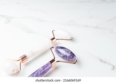 Rose Quartz And Amethyst Face Rollers On Marble Background, Top View. Face Massage Tool, Beauty Treatment And Facial Skin Care Concept.