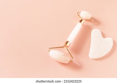 Rose quartz facial massage roller on a pink background. Massage tools with jade stone, anti-aging, anti-wrinkle beauty skincare tool. Copy space.
