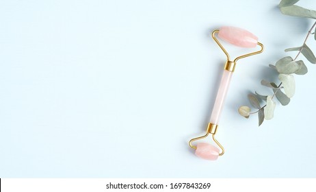 Rose quartz facial roller with eucalyptus leaf on blue background. Jade face massager, anti-aging, anti-wrinkle beauty skincare tool