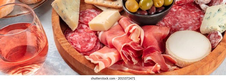 Rose wine with charcuterie and cheese board panorama. Italian antipasti panoramic banner with a wineglass and prosciutto di Parma ham, salami, gorgonzola and olives - Powered by Shutterstock