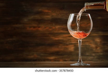 Rose Wine Pouring In Glass On Wooden Background