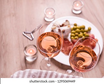 Rose wine and snacks. Two glasses wine on wooden table. Plate green olives, jamon and cheese on a plate. French alcohol drinks with homemade cheese.