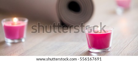 Rose-colored lighted pink candle and rolled brown yoga, pilates mat on the floor ready for workout. Healthy life, keep fit concepts. Focus on candle. Horizontal photo banner for website header design