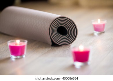 Rose-colored Lighted Pink Wax Candle And Rolled Brown Yoga, Pilates Mat On The Floor Ready For Workout. Close Up. Healthy Life, Keep Fit Concepts. Focus On Mat