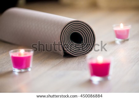 Rose-colored lighted pink wax candle and rolled brown yoga, pilates mat on the floor ready for workout. Close up. Healthy life, keep fit concepts. Focus on mat