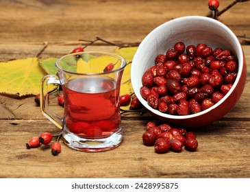 Rosehip tea tea full of vitamins and bowl with dried rosehips.  Autumn mood and colors come from fresh and dried rosehips and november leaves.