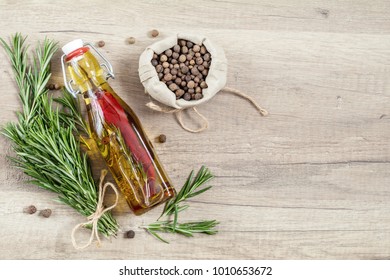 Rosemary bunch of bouquets, olive oil with pepper and spices, fragrant pepper on light wooden surface. Top view, copy space.