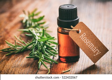 Rosemary essential oil and fresh twig on wooden background. Tag with text rosemary