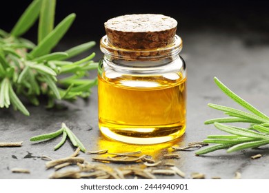 Rosemary essential oil on black texture background with fresh leaves nearby, copy space, natural medicine, organic remedy for hair, skin care, stress therapy