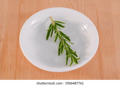 Rosemary herb sprig in a small white bowl placed on to a wooden chopping board