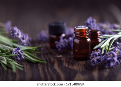 Rosemary And Lavender Essential Oils In Dark Glass Bottles On Wooden Background,  Herbal And Floral Sprigs With Amber Jars. 