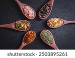 rosemary, pepper, pink salt, mixed chilli seasonings in wooden spoon above the black table