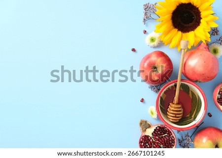 Rosh Hashanah flat lay composition. Top view sunflower, apples, pomegranate, and honey bowl with dipper on blue background.