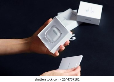 ROSTOV-ON-DON, RUSSIA - Apr.03 2022: Human Hands Unpacking New Model AirPods On The Black Background. The Box From Previous Release Of Apple Earphones Lying Down On Back Stage. Copy Space.