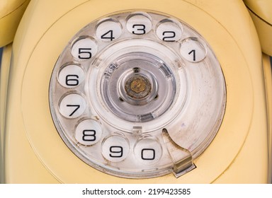 Rotary Dialer Of An Old Telephone With Round Holes And Numbers. Plastic Transparent Dialing Disc On Analog Vintage Landline Phone. Yellow Retro Phone With Handset And Rotary Dial Close Up.