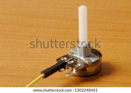 Rotary potentiometer with a yellow wire, on a wooden background