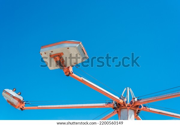 Rotating cars\
and sweeps around center shaft of hurricane ride with cylinder\
piston under sunny blue sky in Dallas, Texas, America. People enjoy\
classic amusement activity in summer\
time