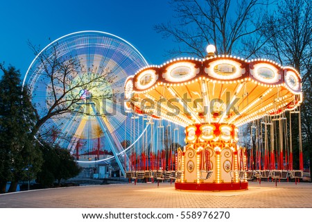 Rotating Illuminated Attraction Ferris Wheel And Carousel Merry-go-round On Summer Evening In City Amusement Park.