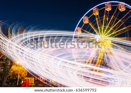 Rotating In Natural Motion Effect Illuminated Attraction Ferris Wheel On Summer Evening In City Amusement Park.