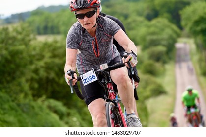 ROTHBURY, NEWCASTLE UPON TYNE, ENGLAND, UK - JULY 06, 2019: An Older Female Cyclist Working Hard Up A Hill In The Cyclone Race Event Starting In Newcastle And Going Through Northumberland.