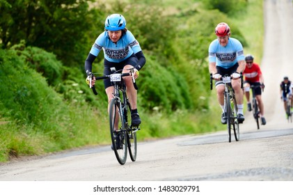 ROTHBURY, NEWCASTLE UPON TYNE, ENGLAND, UK - JULY 06, 2019: An Older Female Cyclist Working Hard Up A Steep Hill In The Cyclone Race Event Starting In Newcastle And Going Through Northumberland.