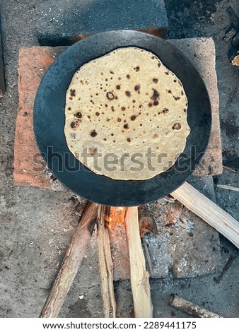 Roti or Indian flat bread is getting cooked on temporary chulha. Top view of a Indian roti Tawa or skillet on the fire.
