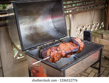 Rotisserie Beef On A Barbecue Closeup Of Rotating Red Meat On Open Grill Outdoors Braai With Juices Dripping From Meat