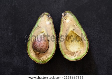 A rotten avocado on a black background. The overripe avocado is cut in half. The core is visible.                             