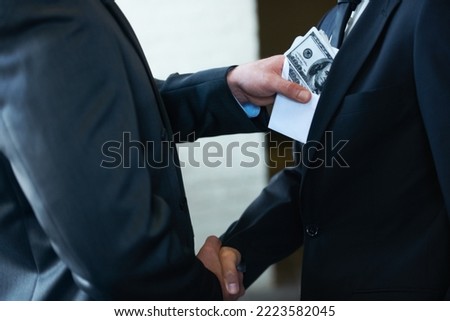 The rotten egg in the corporate world - deceptive deals. Two corporate businessmen shaking hands while one man places money in the otherampamp pocket.