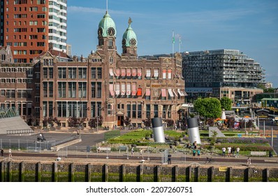 Rotterdam, Netherlands - July 11, 2022: Brown Stone Historic New York Hotel With 2 Green Dome Towers Under Blue Sky On Kop Van Zuid Dock And Quay. People Present In Garden. Other Buildings In Back