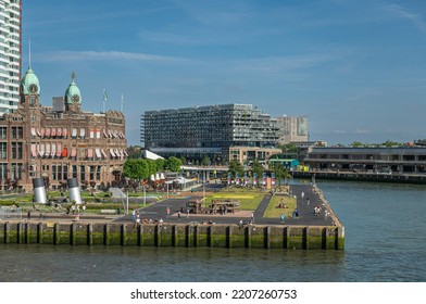 Rotterdam, Netherlands - July 11, 2022: Brown Stone Historic New York Hotel With 2 Green Dome Towers Under Blue Sky On Kop Van Zuid Quay And Dock. People Present In Garden. Other Buildings In Back