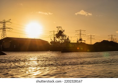 Rotterdam, Netherlands - November 22 2021 : A Highly Polluting Black Coal Power Plant And Power Lines Coming Out Of It At Sunset While Rescue Boat Is Hanging On A Crane