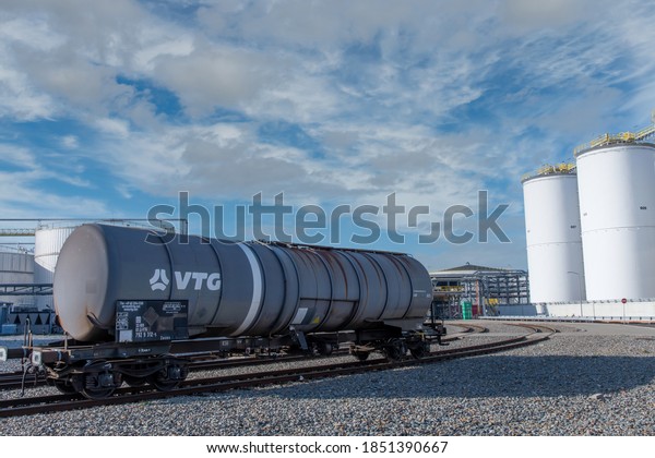 Rotterdam,\
The Netherlands-November 2020; Close up of a chemical car on the\
tracks of a refinery with the white chemical storage tanks in the\
background against a white clouded blue\
sky
