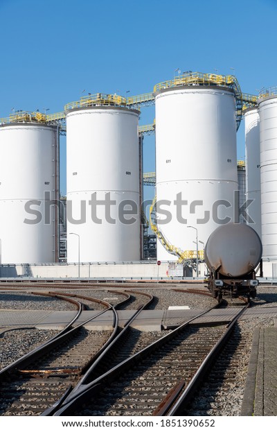 Rotterdam, The Netherlands-November 2020; Vertical\
view down the rial track towards a chemical car on the refinery\
with the white chemical storage tanks in the background against a\
blue sky