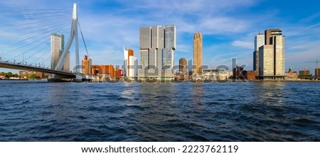 Rotterdam panorama with “Erasmus-Bridge“ spanning over river Nieuwe Maas on a blue sky day in South Holland Netherlands. Silhouettes of tall office buildings, cruise terminal near major at seafront.