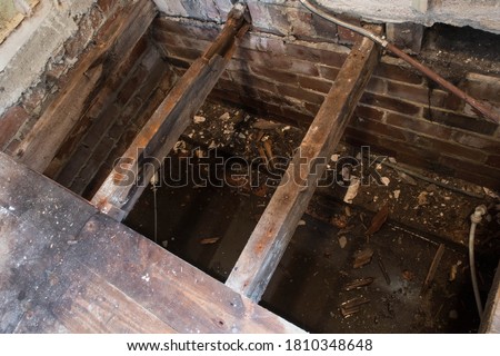 Rotton broken floor joists exposed during home renovation and building works.  View into flooded house foundations.