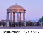 Rotunda and lighthouse on the embankment in the red rays of the rising sun. Summer morning. No people. transparent dome. Granite columns and balustrade. Purple sky. Selective focus.