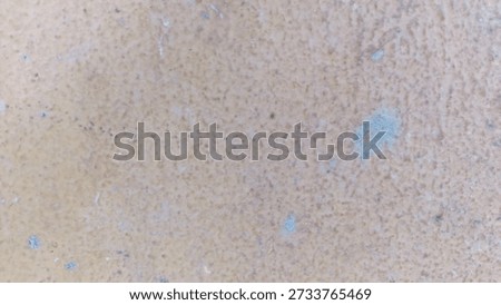 Rough aged surface displays a muted beige and light brown speckled texture with visible small flecks of gray and subtle color shifting across the entirety of the background.