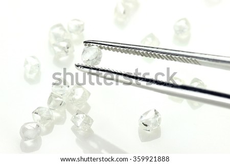 rough diamonds held by tweezers on white background
