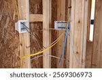 The rough in electrical wiring for outlets and switches in seen between studs in the framing of a new construction house.