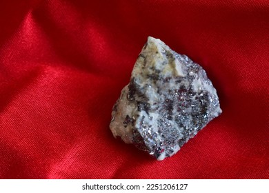 Rough galena on zinnober red background.A closeup of lead glance mineral on day light, mineralogy, geology.Shiny little stone on wrinkled fabric. - Shutterstock ID 2251206127