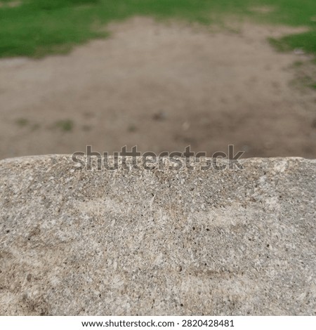 Rough grey concrete stone ledge edge sharply in focus in the foreground with a completely blurred dirt ground behind it